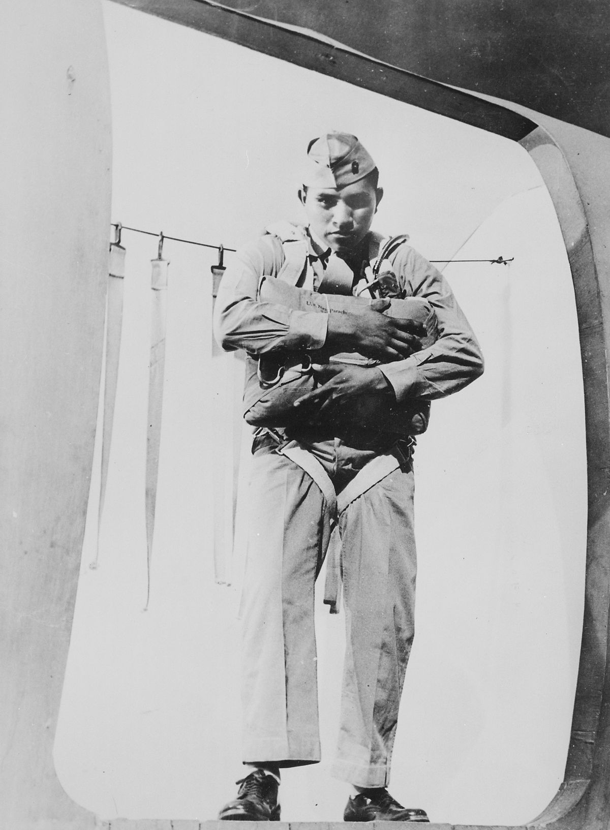 Ira Hayes standing and holding a parachute inside of a plane