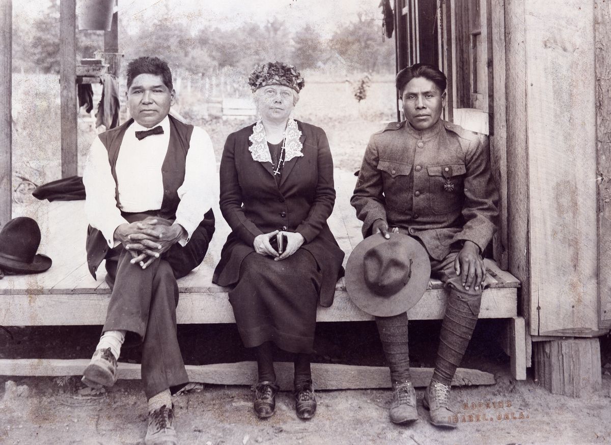 Joseph Oklahombi, in uniform, sitting on a porch alongside John Golombie and Czarina Colbert Conlan