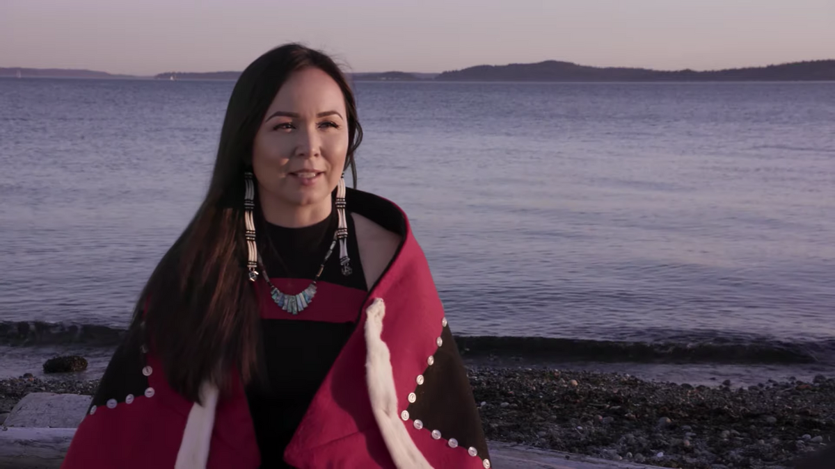 Native American woman cloaked in traditional blanket standing on the beach